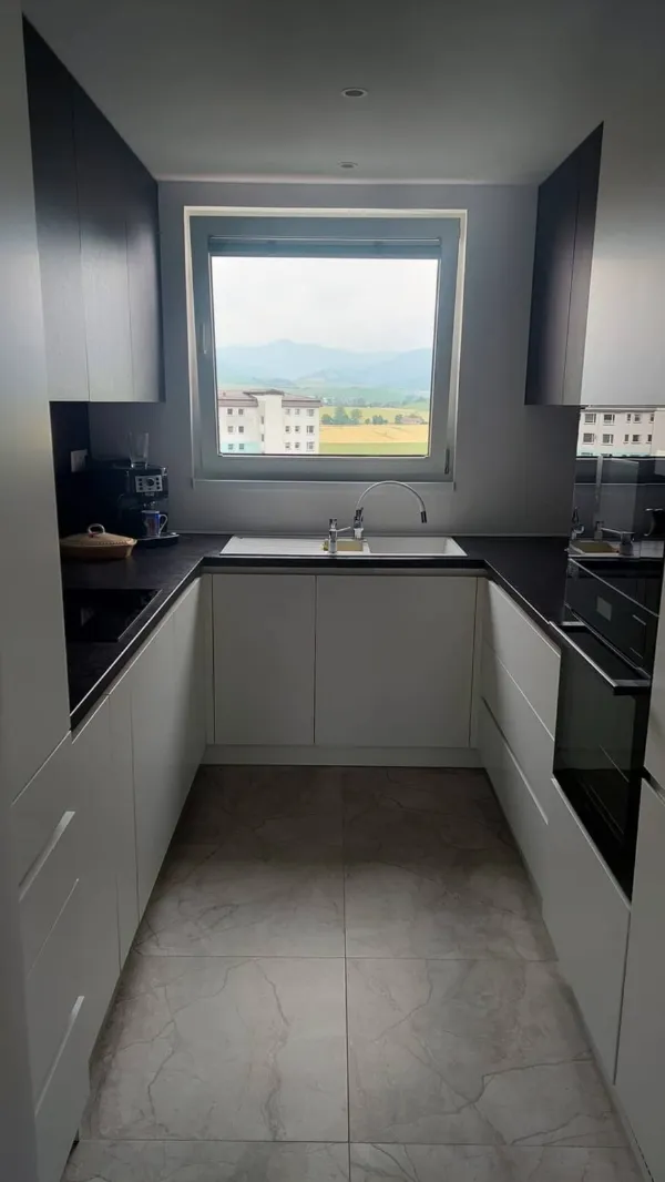 Kuchyňa v tvare U s bielymi dvierkami a čiernou pracovnou doskou pod oknom